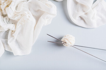 Knitting needles stick out from a ball of yarn and knitted fabric nearby on a blue top view