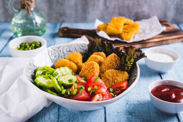 Bowl with crispy nuggets, tomato and cucumber on the table