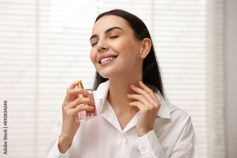 Sticker Smiling woman spraying aromatic perfume at home