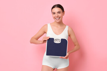 Diet and weight loss concept. Happy young woman with floor scale on pink background