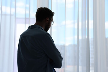 Loneliness concept. Sad man near window at home, back view. Space for text