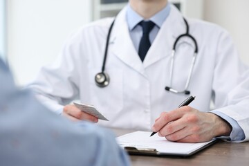 Doctor writing prescription for patient at wooden table in clinic, closeup