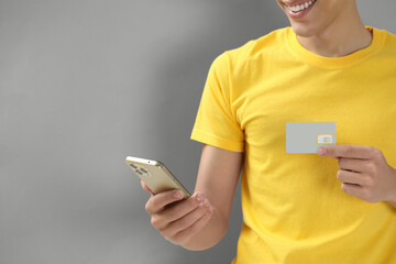 Man holding SIM card and smartphone on grey background, closeup. Space for text