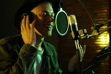 Vocalist with headphones singing into microphone in professional record studio