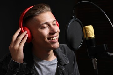 Man wearing headphones singing into microphone in professional record studio