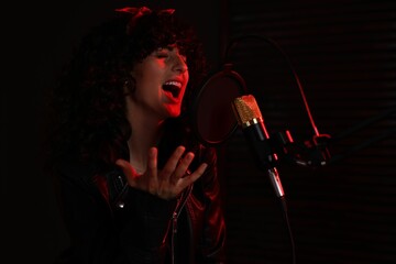 Vocalist singing into microphone in professional record studio with red light