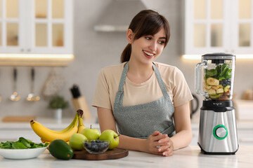 Young woman making delicious smoothie with blender at white marble table in kitchen