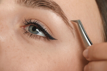 Naklejka premium Beautician plucking young woman's eyebrow, closeup view