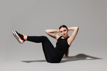 Young woman doing aerobic exercise on light grey background
