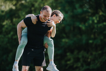 Smiling couple having fun during an outdoor exercise session in the park, enjoying a piggyback ride...