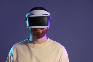 Smiling man using virtual reality headset on dark purple background. Space for text