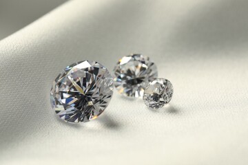 Three beautiful shiny diamonds on white fabric, closeup