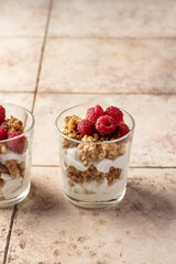 Berry dessert in glass with granola, fresh raspberries, yogurt or cream cheese. Healthy breakfasr concept, on beige tile background with text space