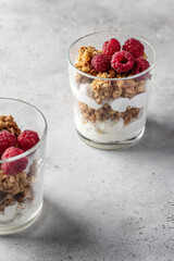 Berry dessert in glass with granola, fresh raspberries, yogurt or cream cheese. Healthy breakfasr concept, vegetarian on gray background