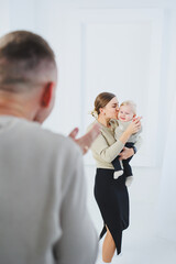 Young parents mom and dad are playing with a baby on a white background. A married couple hugs their newborn son. A happy family.