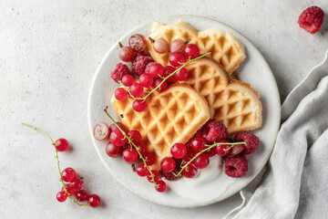 Homemade waffles with summer berries and a scoop of ice cream in plate on grey table top view. Heart shaped waffles