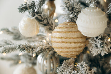Elegant white and gold bauble on a frosted Christmas tree, illuminated by twinkling lights. The intricate details and sparkling accents add a touch of luxury to the festive decor