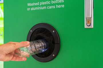 Man puts plastic bottle in a reverse vending machine. Male hand inserting reusable bottle into...
