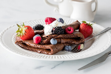 Folded chocolate crepes topped with whip cream and fresh berries.