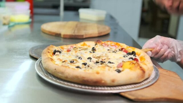 A chef checks whether the pizza is baked by removing it from a hot fryer and transferring it to a wooden board to serve to a client in a pizzeria restaurant.