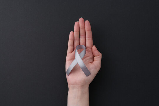 Woman with grey awareness ribbon on black background, top view