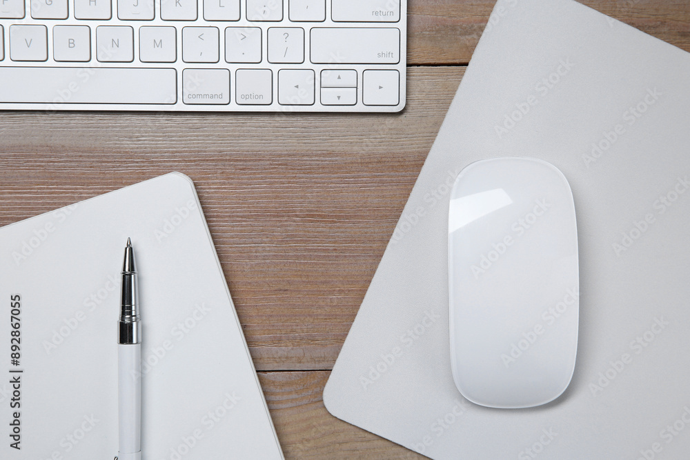 Wall mural wireless mouse with mousepad, notebook, pen and computer keyboard on wooden table, flat lay