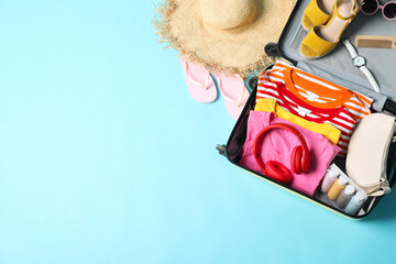 Open suitcase with traveler's belongings on light blue background, flat lay. Space for text