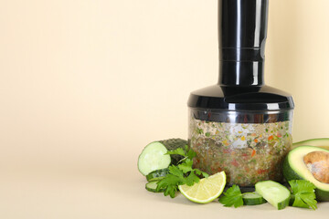 Hand blender with mixture of ingredients and fresh products on beige background, space for text