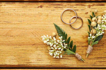 Small stylish boutonnieres and rings on wooden table, flat lay. Space for text