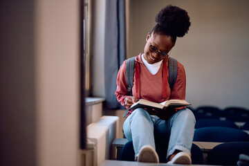 Happy black student learning from  book in classroom.