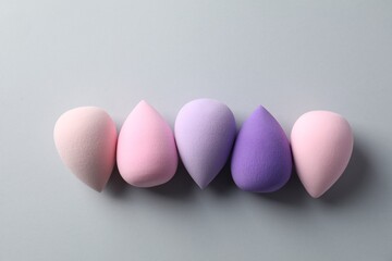 Many colorful makeup sponges on grey background, flat lay
