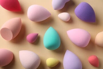 Many colorful makeup sponges on beige background, flat lay