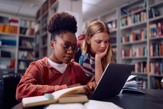 Black college student and her female friend using laptop while learning in library.