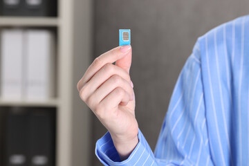 Woman holding SIM card indoors, closeup view