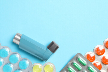 Asthma inhaler and pills on light blue background, flat lay. Space for text