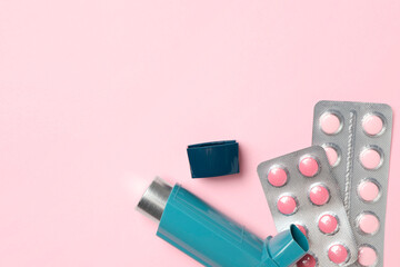 Asthma inhaler and pills on pink background, flat lay. Space for text