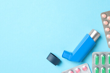 Asthma inhaler and pills on light blue background, flat lay. Space for text