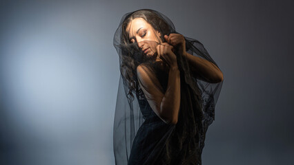 A Gothic bride, a mysterious Halloween image, a Gothic gloomy aesthetic. An elegant young woman in a black dress and with a veil on her face