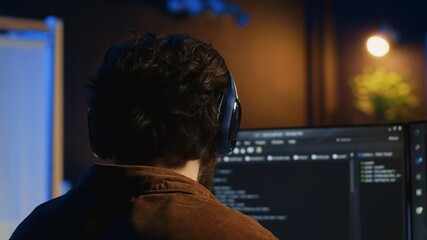 Technician putting headphones on while using coding to fortify firewalls, teleworking for IT...
