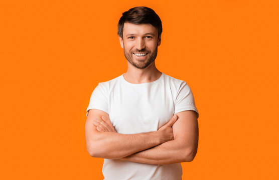 A man smiles with his arms crossed while standing in front of an orange background.