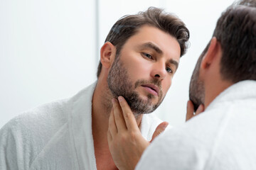 Obraz premium Close-up male wrinkles. Portrait of brunet man touching skin wrinkles. Middle aged man with touch wrinkles in front of the mirror. Aged skin. Man 40s cosmetic, skin treatment. Male face with wrinkles.