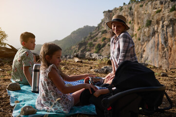 Family enjoying a picnic outdoors in a mountainous area with children and a baby