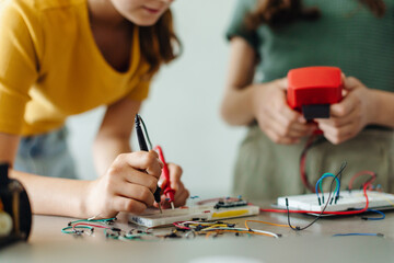 School girls working on circuit board of small robot, building robotic car in after-school robotics...