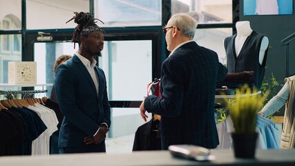 Senior designer teaching his apprentice to match ties on elegant suits, presenting the color mixing...