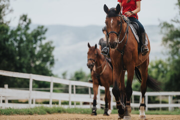 Two individuals riding horses on a rural path surrounded by fences and scenic mountain views. The riders are enjoying a leisurely outdoor activity on a beautiful day.