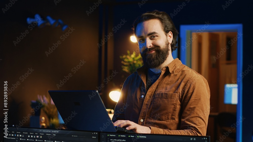 Poster portrait of smiling man doing it support job from home, standing in personal office with laptop in h