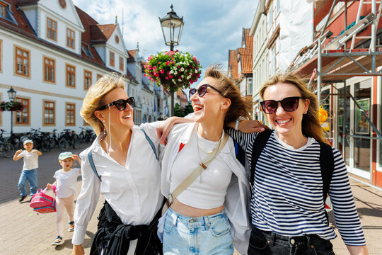 Three cheerful young adult women friend with kids walk street old european german town city street enjoy having fun laughing sunny day together. Female persons friendship celebration party weekend