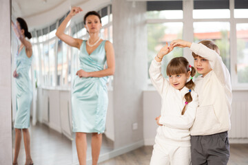 Couple of boy and girl kids dressed in sport wear twirling while taking hustle dancing lessons.