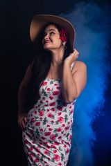 Portrait of beautiful smiling young woman with black hair wearing brown hat with colorful clothes and a red flower in her ear.