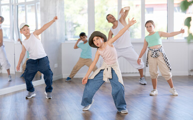 Happy enthusiastic teen girl honing hip-hop moves in modern dance studio setting with group of...